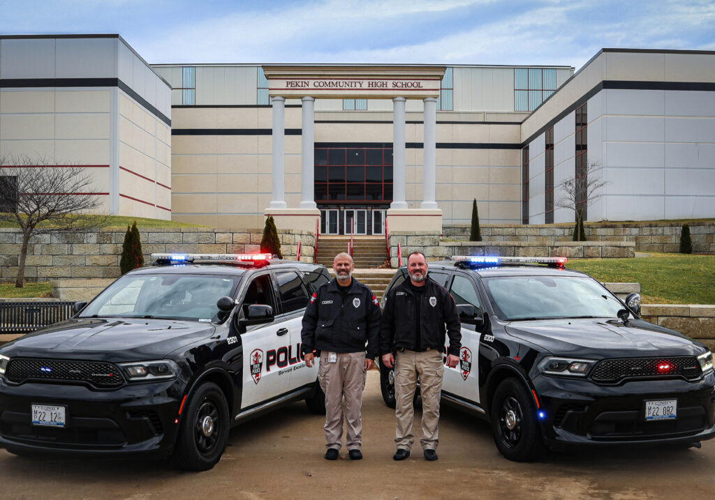 Two school resource officers next to their vehicles in from of school building.